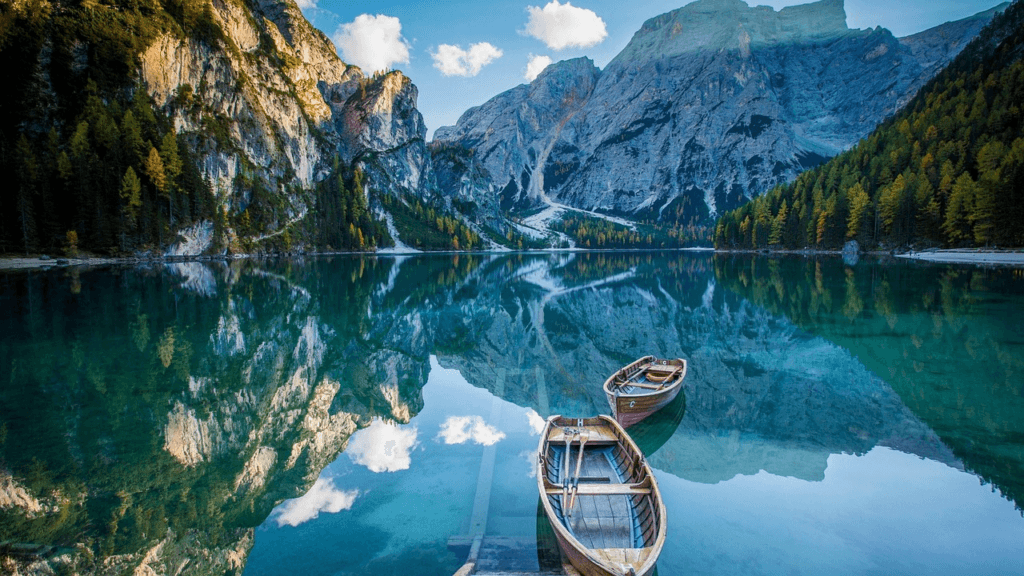 Serene mountain lake with two wooden boats floating on crystal-clear water, reflecting the peaceful landscape – representing the journey to be at peace with yourself and find freedom from inner struggles.